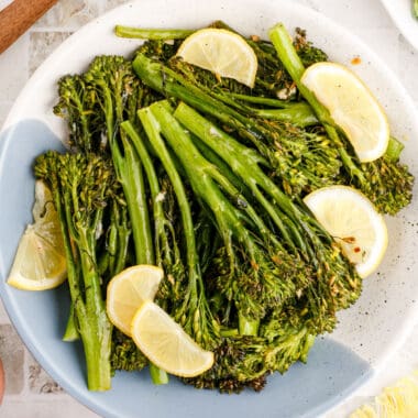 square image of lemon butter broccolini with lemon slices in a bowl