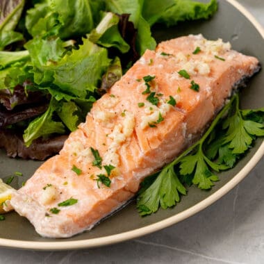 square image of lemon garlic butter baked salmon filet on a plate with a green salad