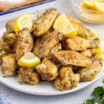 square image of lemon pepper wings piled on a plate with lemon slices and chopped parsley