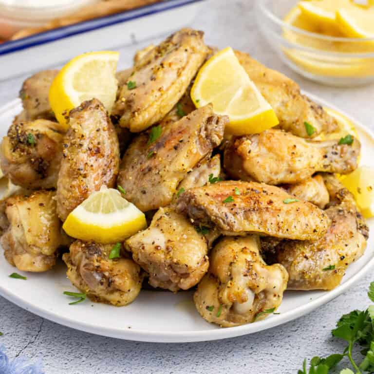 square image of lemon pepper wings piled on a plate with lemon slices and chopped parsley