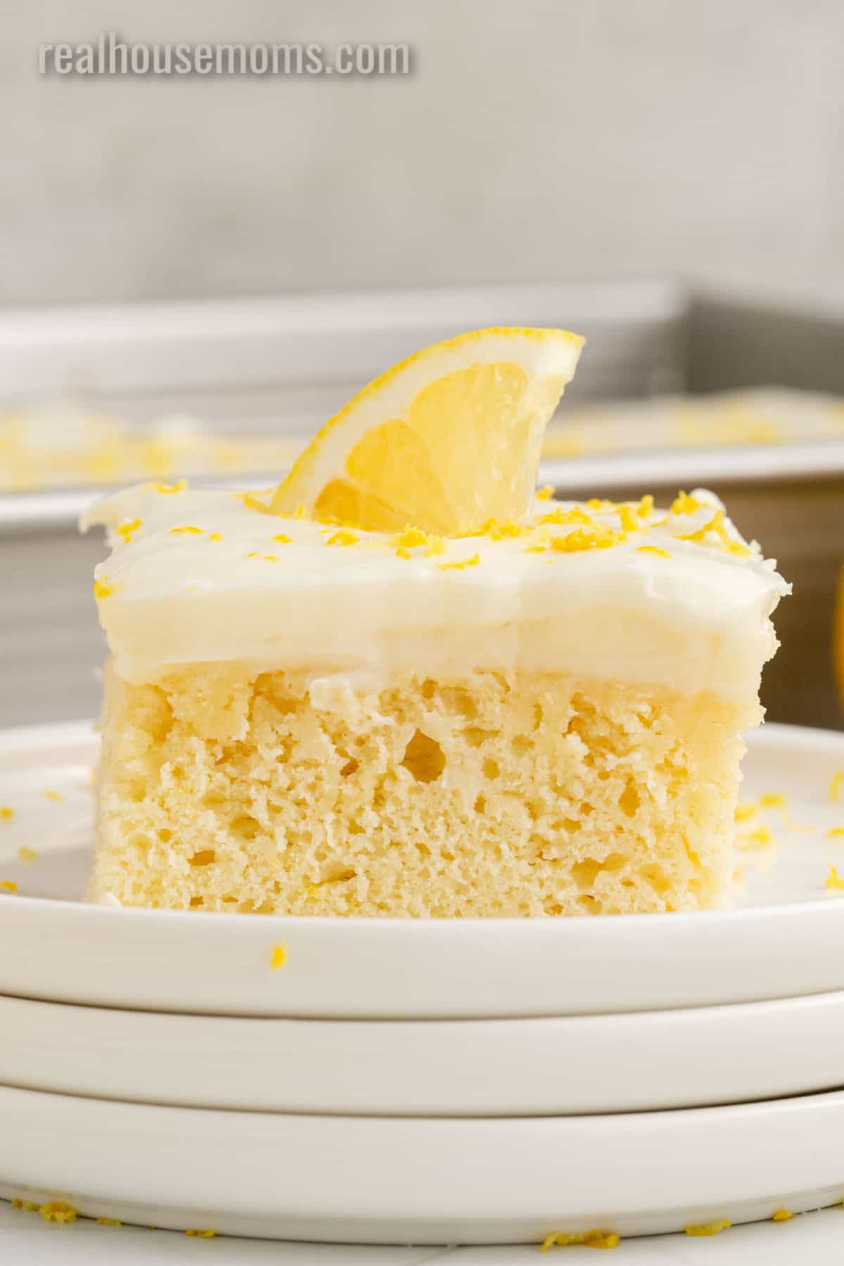 side view of lemon poke cake topped with lemon zest and a quarter slice of lemon