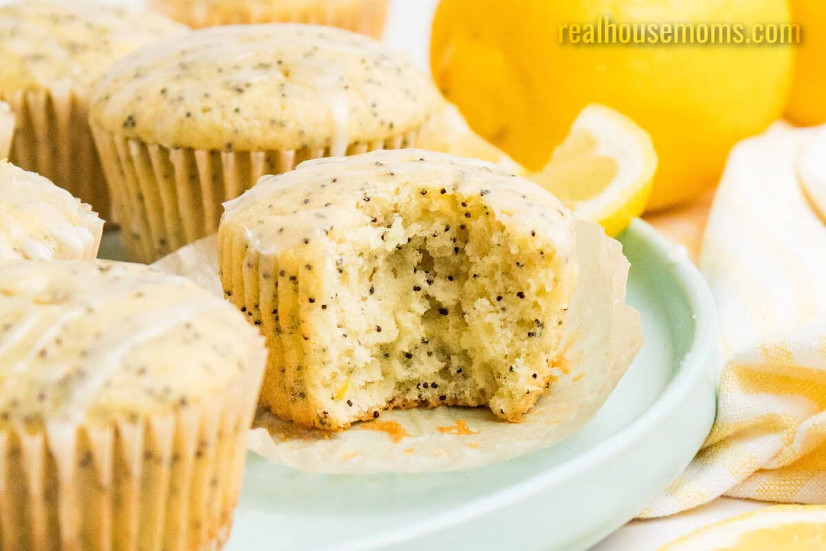 lemon poppy seed muffins on a plate with a bite taken out of one to show the texture inside