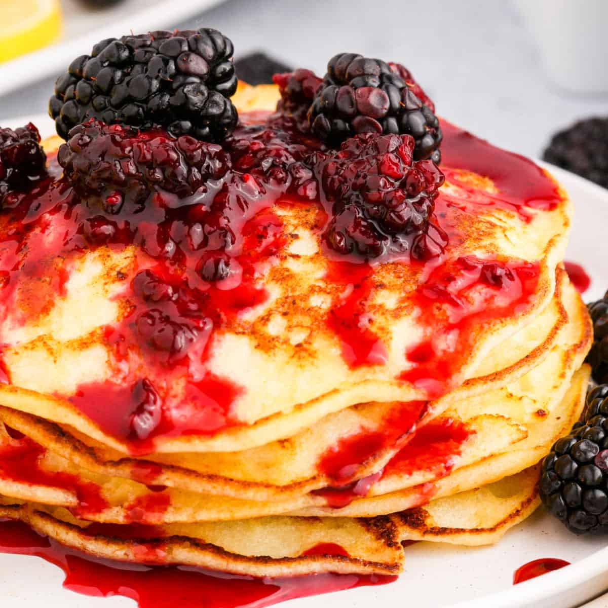 square image of a stack of lemon ricotta pancakes topped with homemade blackberry sauce