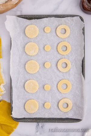 linzer cookie cutout on a parchment lined baking sheet with the small cutouts next to the big cookies