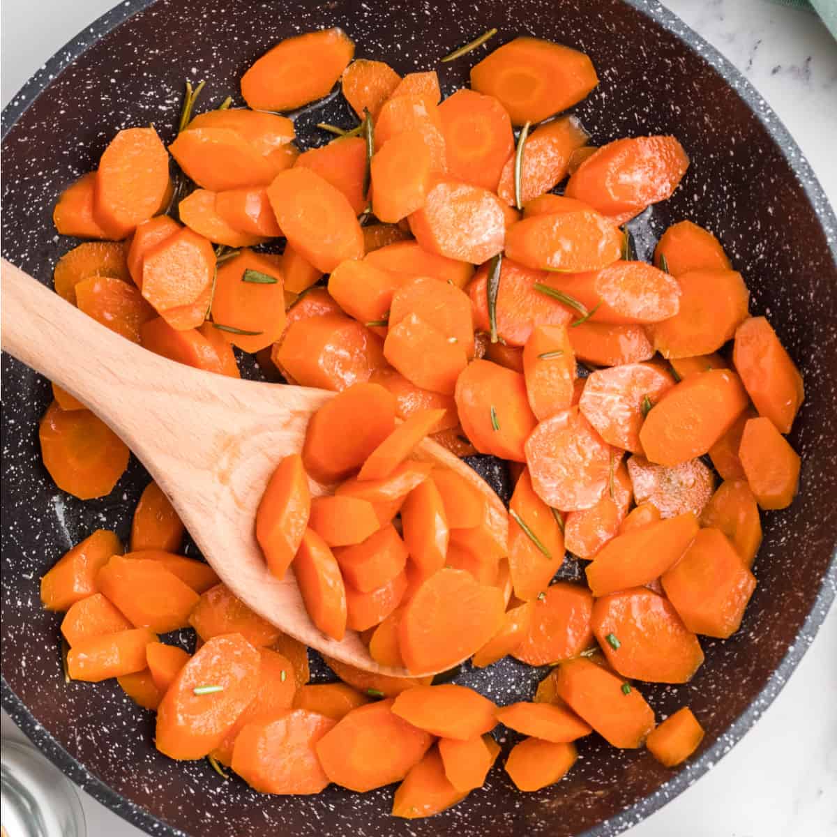 square image of Liz's candied carrots in a skillet with a wooden spoon