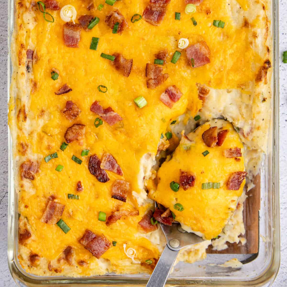 square image of a serving spoon in a casserole dish of loaded mashed potato casserole