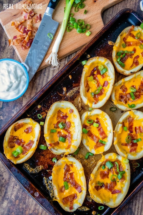 loaded potato skin on a baking sheet topped with cheese, bacon, and green onions
