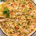 square image of lobster alfredo in a skillet with lemon wedges for garnish