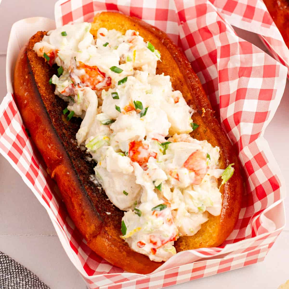 square image of a lobster roll in a tray with deli paper