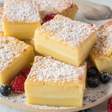 square image of magic custard cake slices on a plate with fresh berries