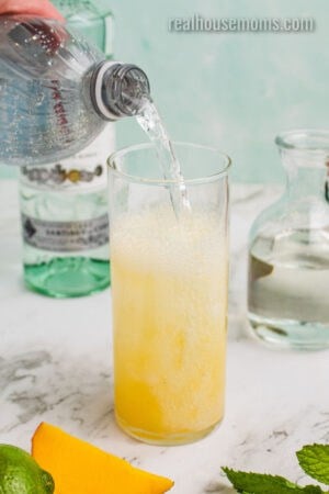club soda being poured into a glass with mango mint puree and ice