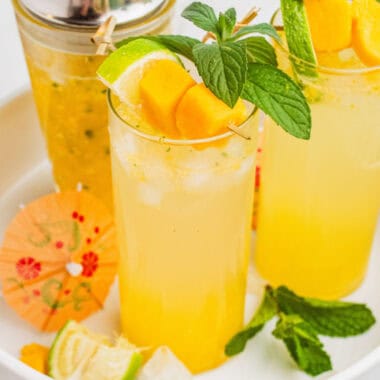 square image of two mango mojitos on a white tray next to the cocktail shaker