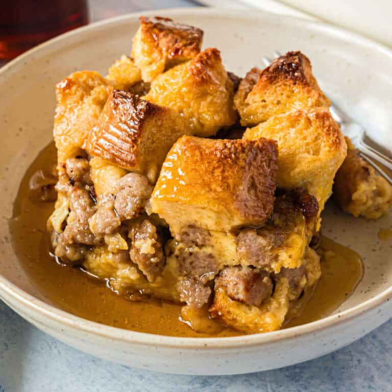 square image of a portion of maple sausage french toast bake on a plate, topped with syrup