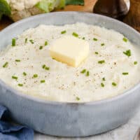 recipe card picture of mashed cauliflower in a grey bowl with a slice of butter on top