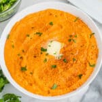 square image of mashed sweet potatoes in a serving bowl with cinnamon, parsley, and butter on top