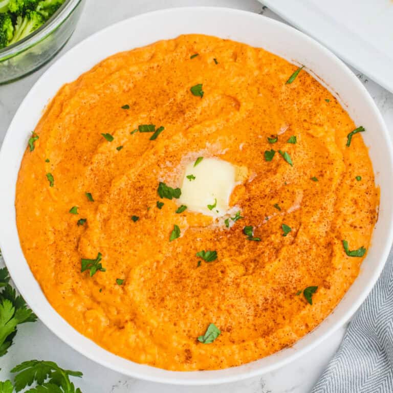 square image of mashed sweet potatoes in a serving bowl with cinnamon, parsley, and butter on top