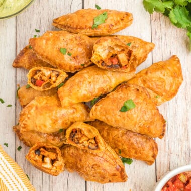 square image of mexican chicken empanadas piled up with two broken in half to show filling inside