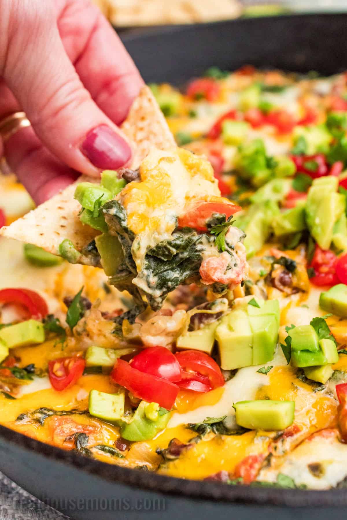 hand holding tortilla chip dipped in mexican spinach dip over the skillet