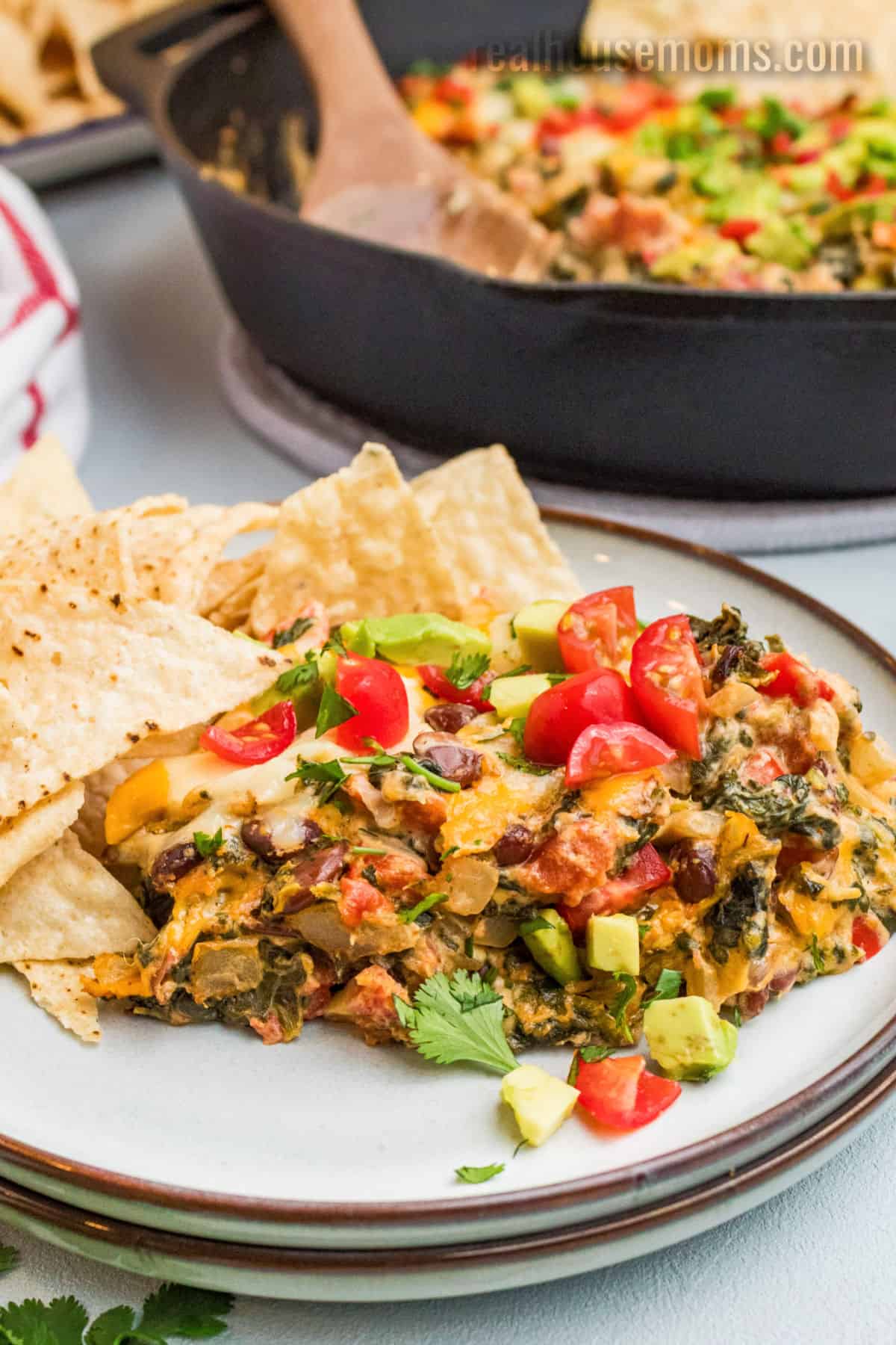 portion of mexican spinach dip on a small plate with tortilla chips next to the skillet