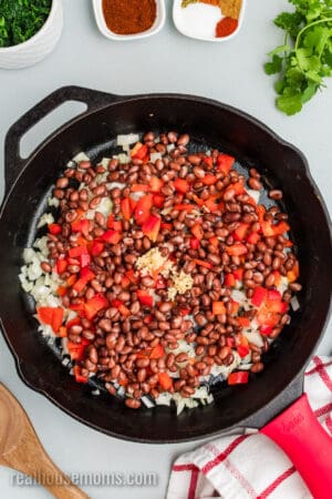 onions, garlic, bell peppers, and black beans in a cast iron skillet