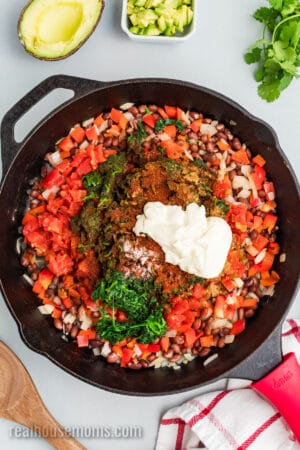 rotel, spinach, seasonings, and mayonnaise added to a skillet of sautéed veggies and black beans