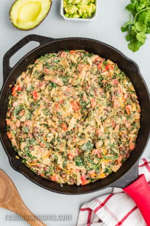 veggies for mexican spinach dip mixed with cream cheese, cheddar, and pepper jack and spread into an even layer in a cast iron skillet