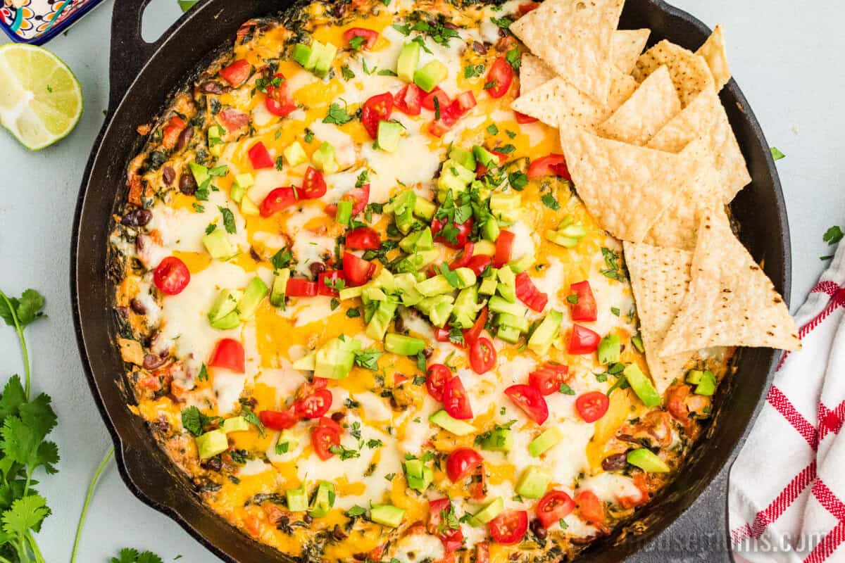 looking down at a skillet of mexican spinach dip topped with diced avocado, tomato and chopped cilantro