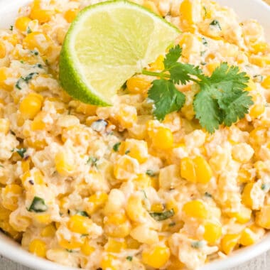 square close up image of mexican street corn dip in a bowl topped with cilantro and a lime wedge