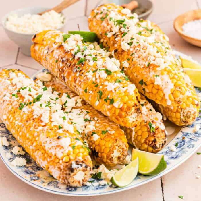 square image of Mexican Street Corn piled on a serving platter with lime wedges