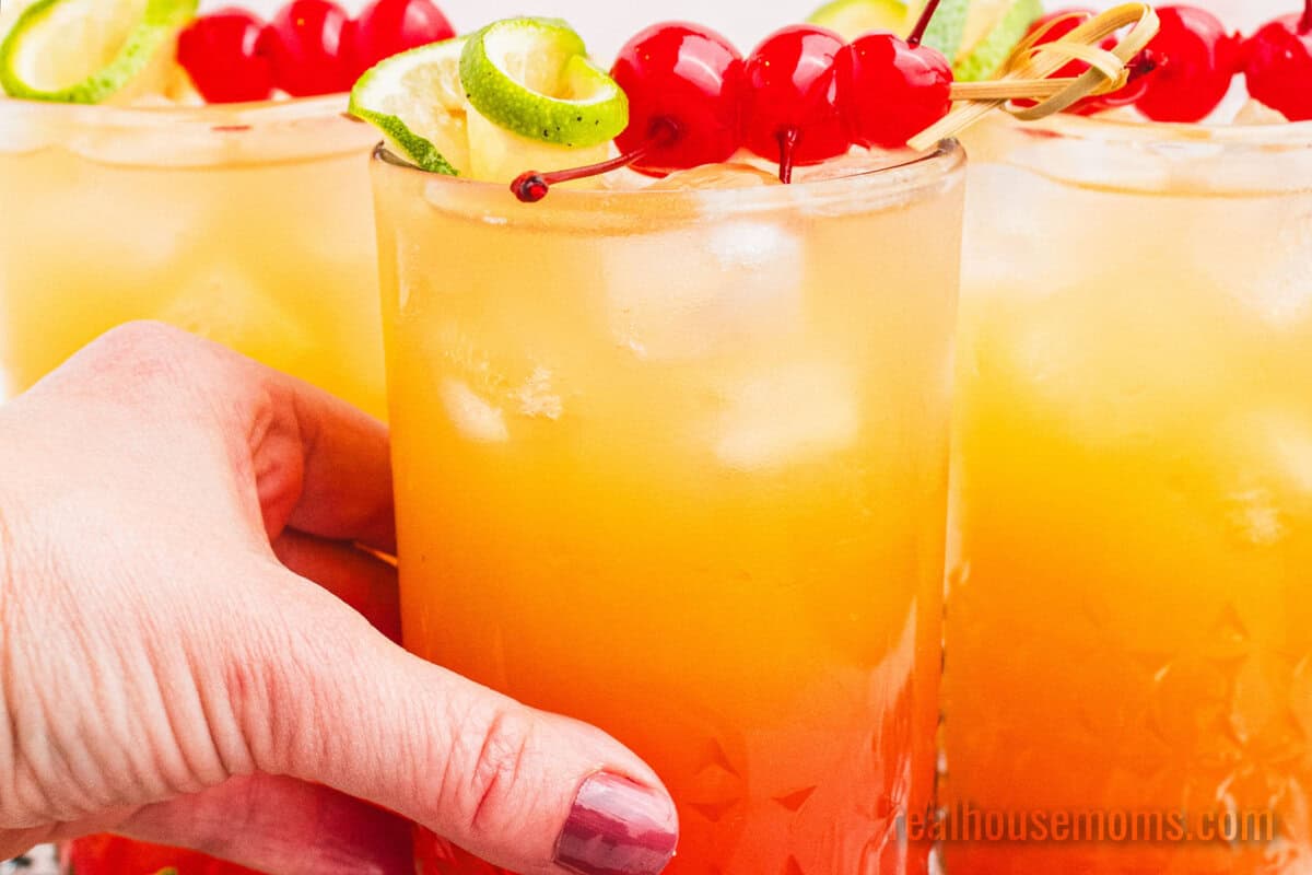 hand grabbing a tequila sunset from a group of cocktails