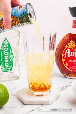 pineapple juice being poured into a glass cocktail shaker with ice, tequila, and liqueurs