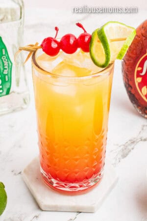 mexican sunset garnished with a lime slice and cherries on a cocktail pick