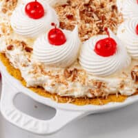 million dollar pie topped with whipped cream and cherries in a pie plate with recipe name at the bottom