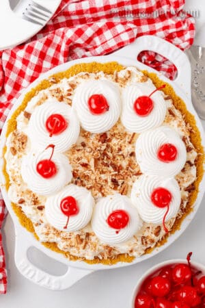 looking down at a whole million dollar pie topped with whipped cream swirls and cherries in a pie plate