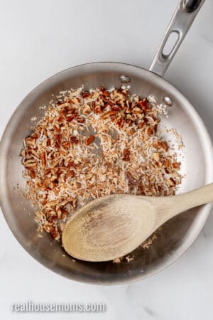 toasted chopped pecans and shredded coconut in a small skillet with a wooden spoon