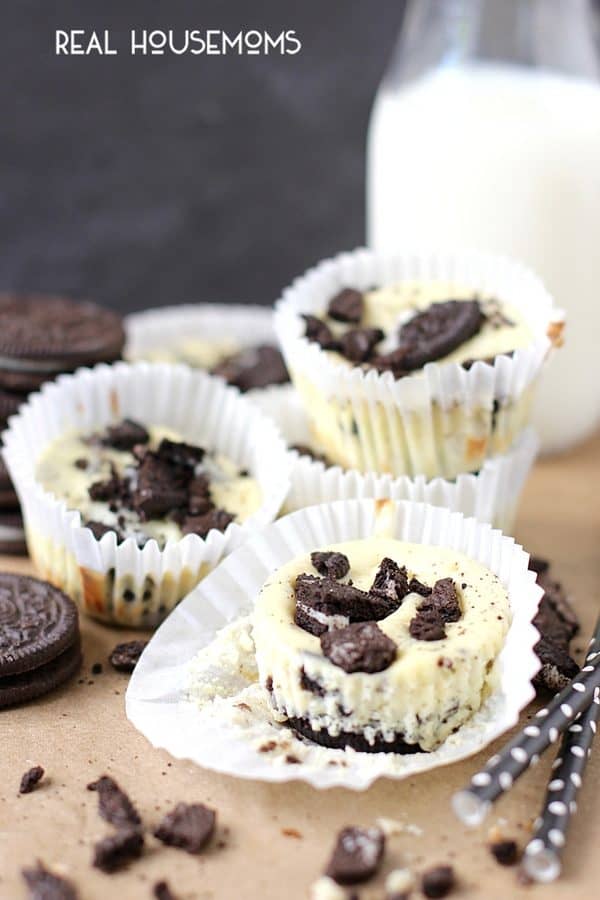 Mini Oreo Cheesecakes topped with chopped Oreos with the cupcake liner undone so you can see the layers