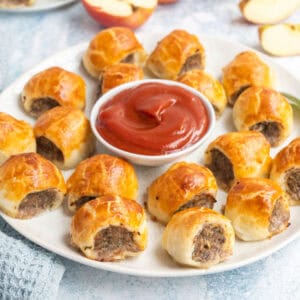 square image of mini pork, apple & sage sausage rolls on a plate with curry ketchup