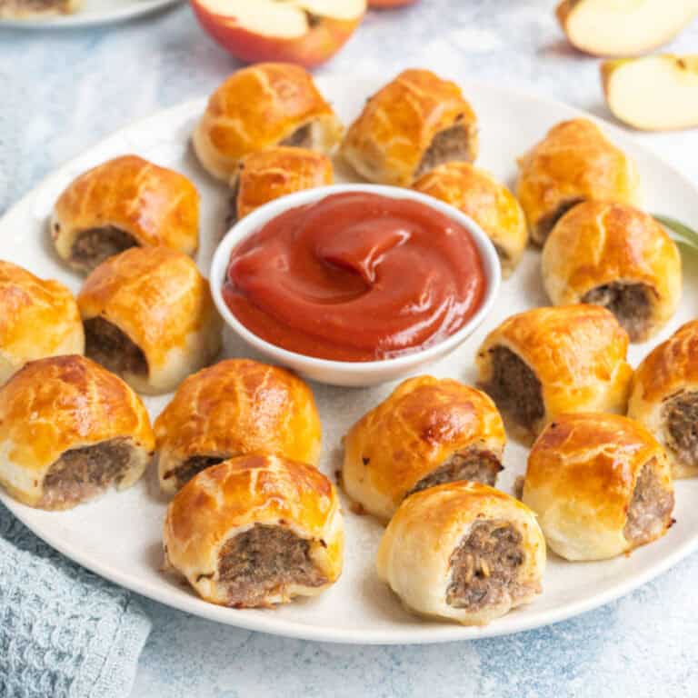 square image of mini pork, apple & sage sausage rolls on a plate with curry ketchup