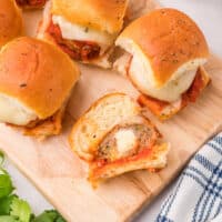 mozzarella stuffed meatball sliders on a board with one cut in half to show filling with recipe name at the bottom