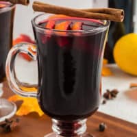 Image of a clear glass filled with Mulled wine with orange slices and a cinnamon sticks on top
