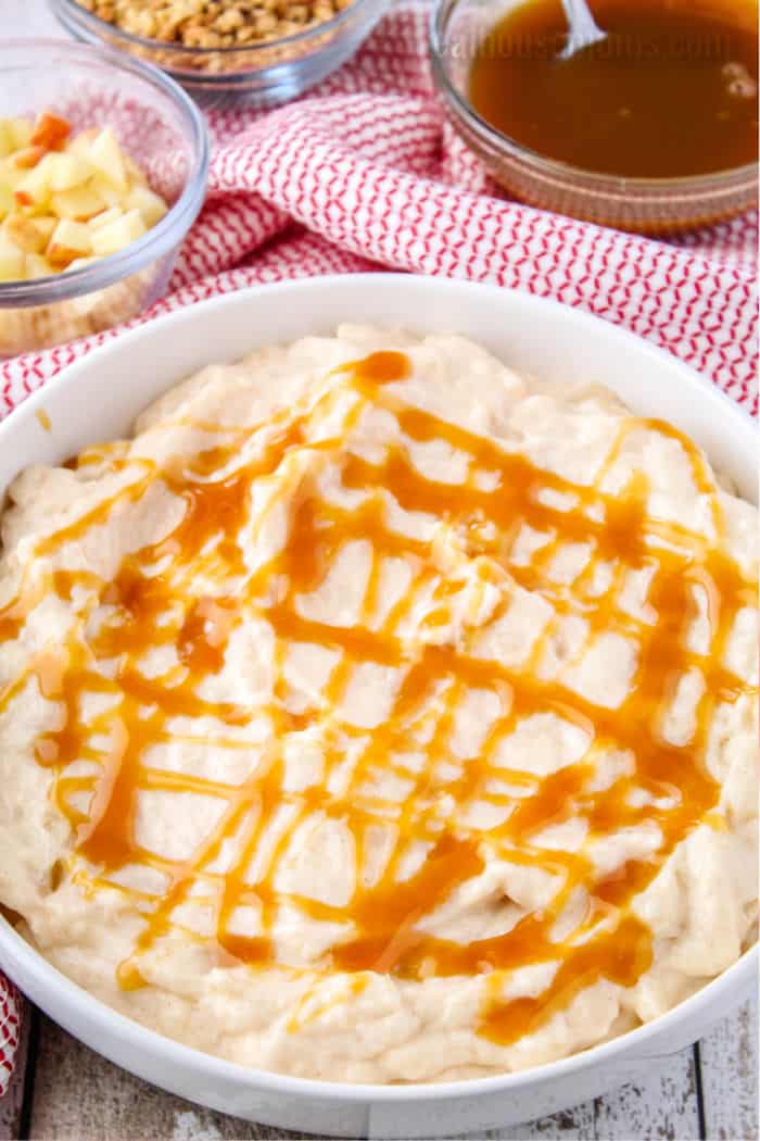 no bake apple cheesecake dip in a shallow bowl with caramel sauce drizzled over the top
