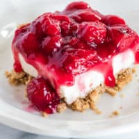 cheesecake on a white plate with cherry topping and graham cracker crust.