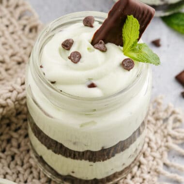 square image of no bake mint chocolate chip cheesecake with chocolate chips, Andes mint, and mint sprig for garnish