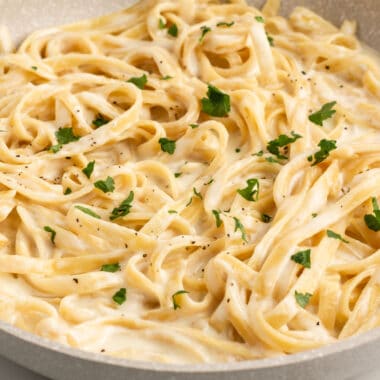 square close up image of one pot alfredo pasta in a skillet with chopped parsley on top