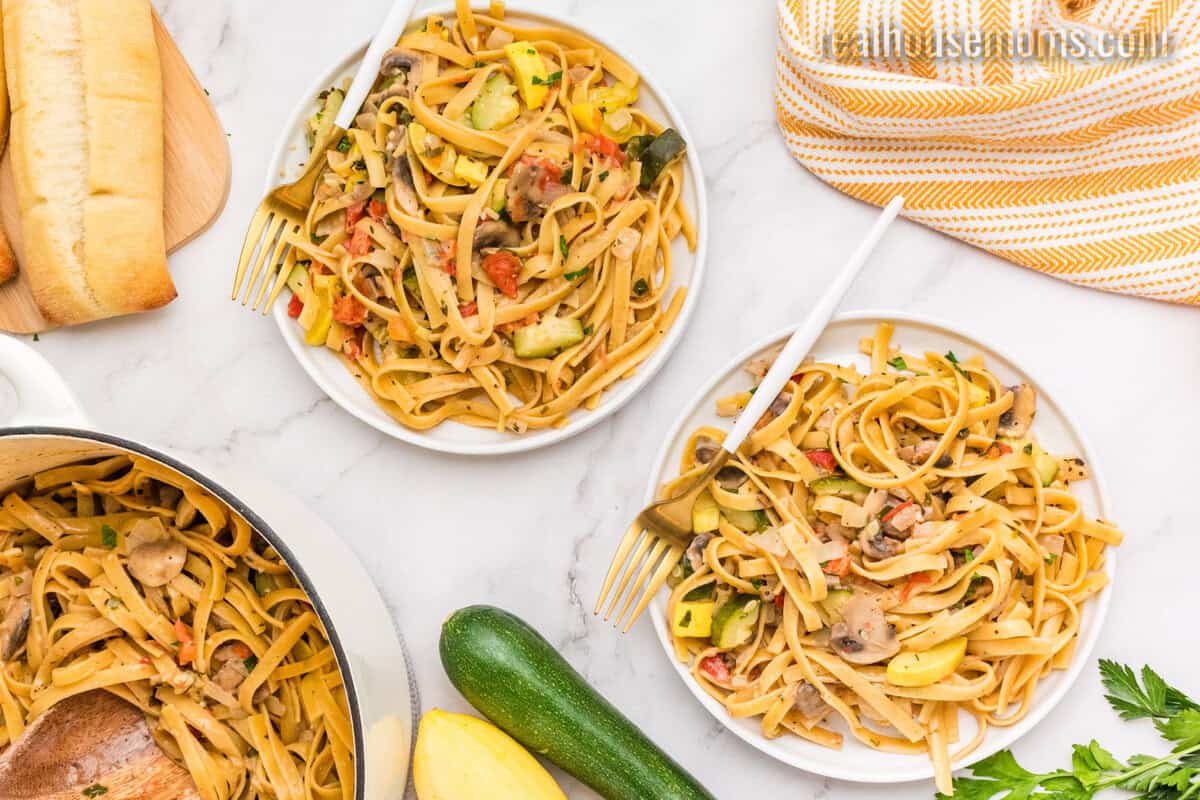two plates of one pot summer vegetable pasta next to a loaf of crusty bread