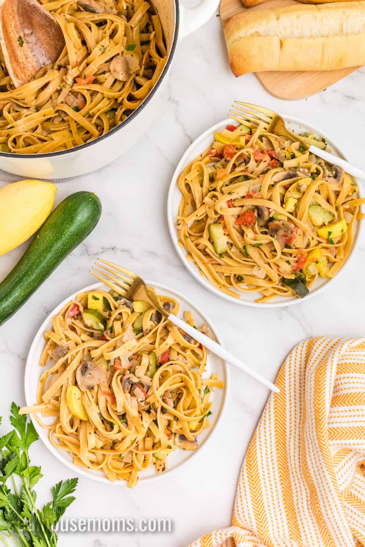 two plates of one pot vegetable pasta with forks next to the pot and some crusty bread