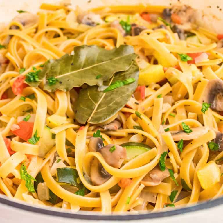 square image of one pot vegetable pasta in a dutch oven with bay leaves on top