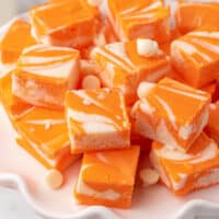 square image of orange creamsicle fudge piled up on a scalloped plate