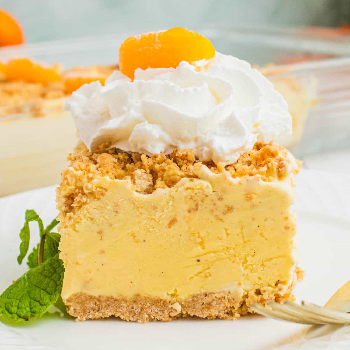 square image of a slice of orange creamsicle ice cream dessert topped with whipped cream and a mandarin orange