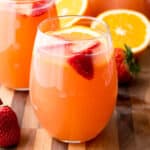 square image of orange strawberry rose sangria on a cutting board in a stemless wine glass